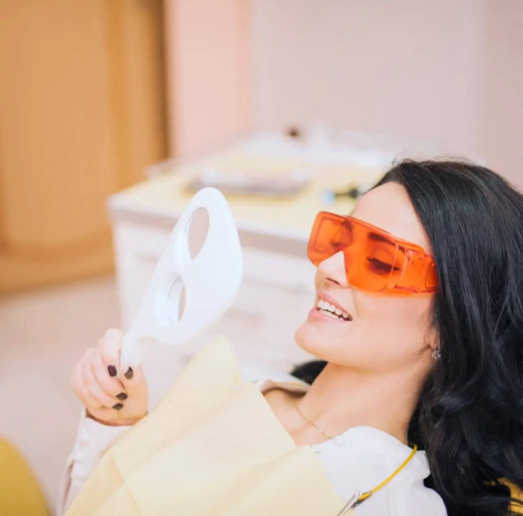 Paciente sorrindo e olhando no espelho após tratamento de lentes de contato dental em porcelana em Jundiaí na clínica Oral Mac.