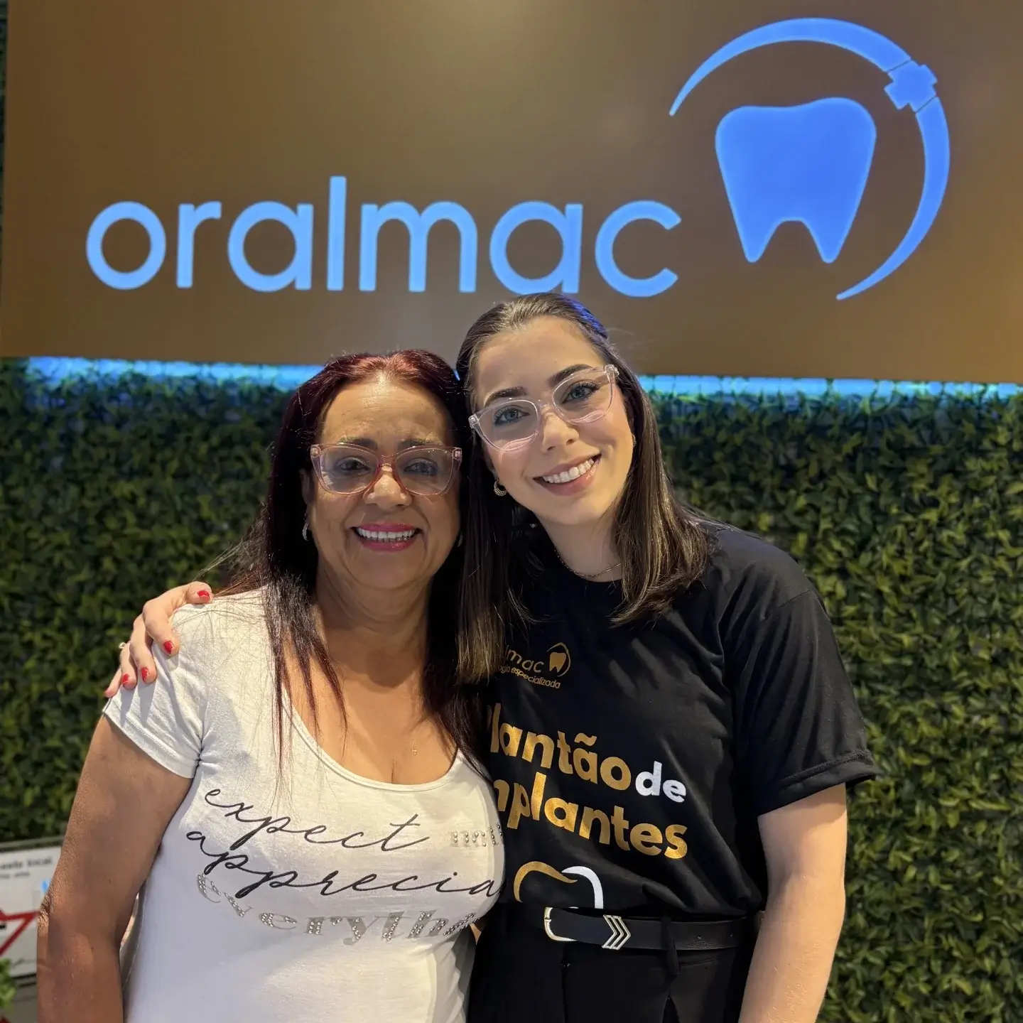 Especialista da Oral Mac e paciente sorrindo em frente ao logo da clínica, referência como dentista em Jundiaí.