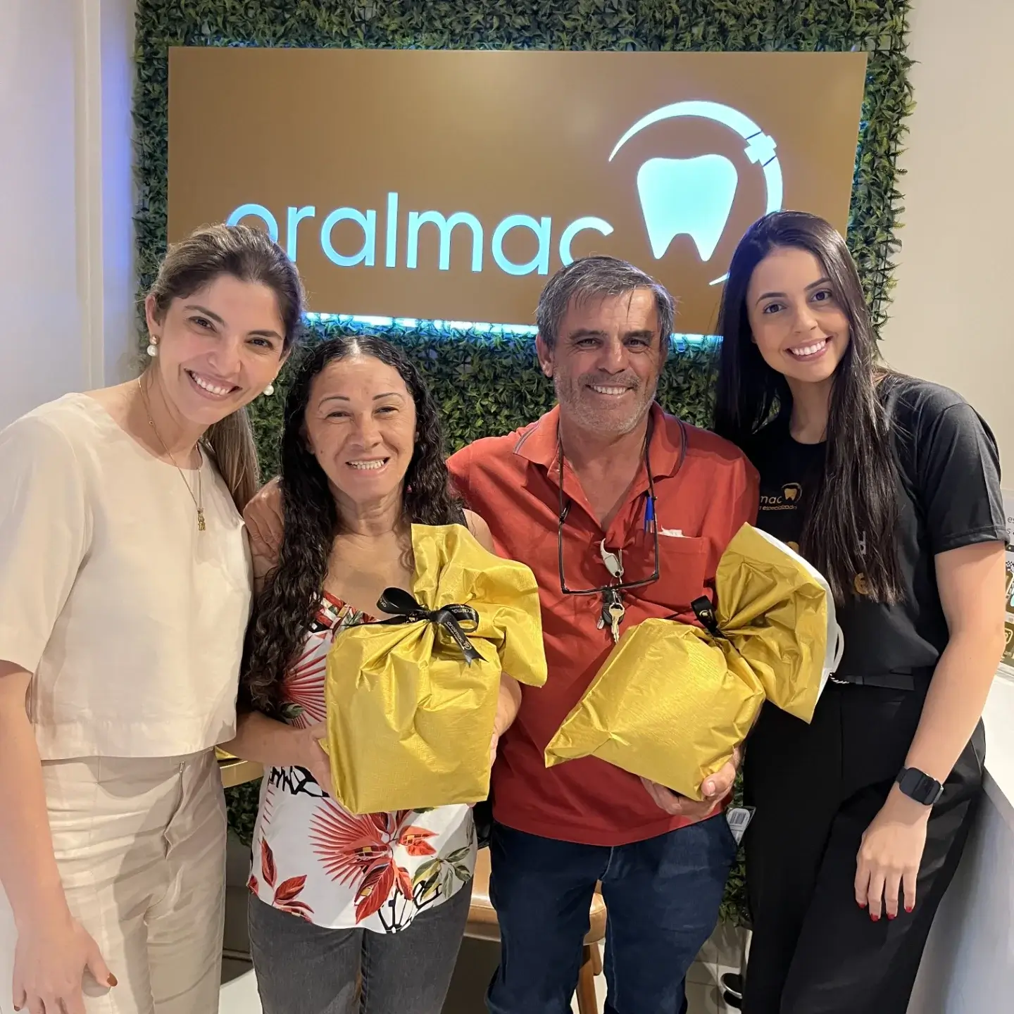 Dentista em Jundiaí da clínica Oral Mac sorrindo ao lado de pacientes satisfeitos em momento de entrega de mimos.