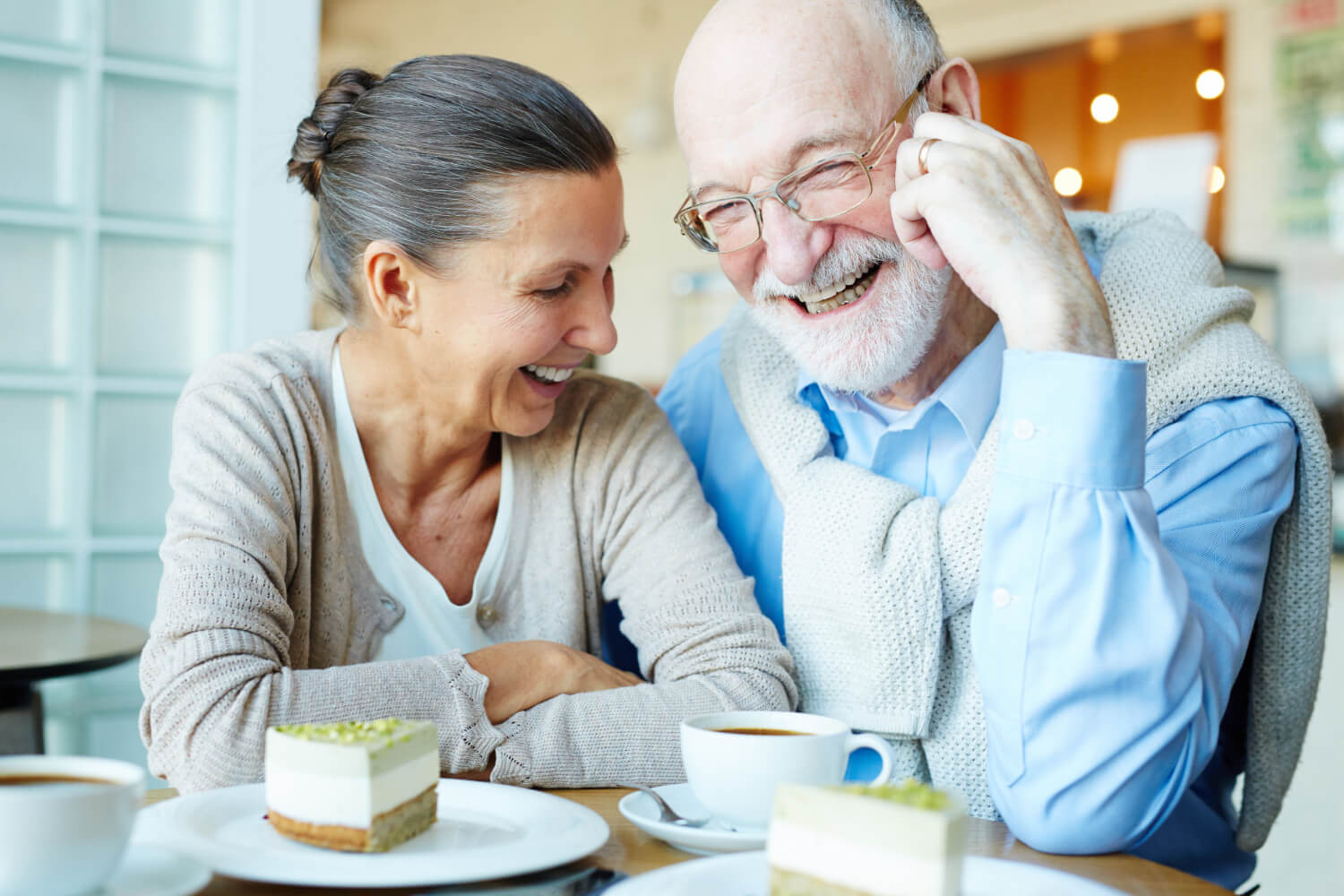 Casal de idosos sorrindo em um café, refletindo a alta durabilidade da prótese protocolo feita na Clínica Oral Mac em Jundiaí